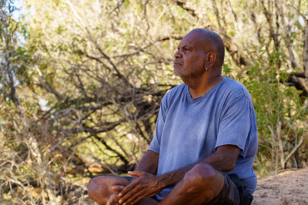 A man sitting down on the ground with his legs crossed, staring into the distance.