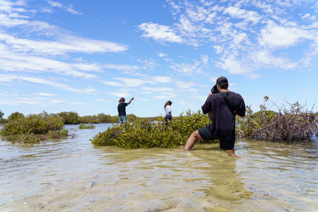 A videographer filming two girls fishing in shallow waters at Bush Bay
